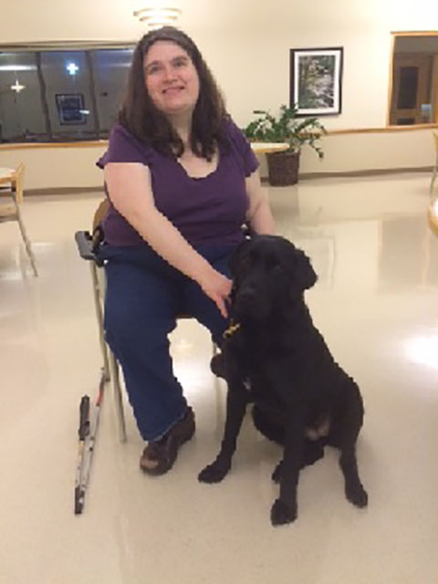 Photo of Tristen and her guide dog Kiowa. Kiowa is a 58 pound, black, Labrador-Retriever, with a triangular white patch of fur on her chest.